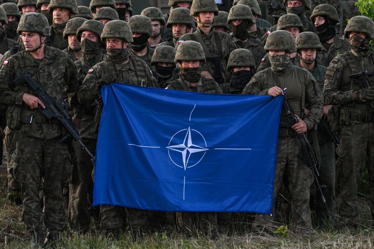 ORZYSZ, POLAND - JULY 03: Polish soldiers hold a NATO flag during a family photo after a training demonstration with the NATO multinational battle group eFPon at the Orzysz training ground on July 03, 2022 in Orzysz, Poland. The multinational battlegroup here is one of eight such battalions that NATO has stationed in countries along its eastern flank, from the Baltic Sea to the Black Sea. (Photo by Omar Marques/Getty Images)