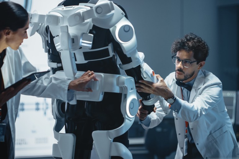 In Robotics Development Laboratory: Chief Female Engineer and Top Male Scientist Work on a Bionics Exoskeleton Prototype. Designing Powered Exosuit to Help Disabled People Walk, Workers Lift Goods; Shutterstock ID 1837865782; purchase_order: aljazeera ; job: ; client: ; other: