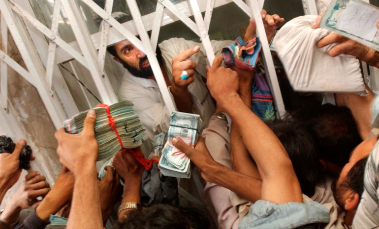 KABUL, AFGHANISTAN - OCTOBER 9: Afghan men desperately attempt to turn in old Afghan bills for new ones in the main money bazaar October 9, 2002 in Kabul, Afghanistan. Afghanistan introduced a new currency on Monday, sending hoardes of Afghans to the money exchanges to turn in the old currency for the new one. The old Afghan money's highest denomination of 10,000 Afghanis was worth about a quarter in U.S. dollars, necessitating huge stacks of cash for most transactions. The old currency, once turned in, is destroyed. The new currency is critical for the government to take control over Afghanistan's chaotic monetary policy, which up to now included money printed by regional warlords. Old money can be exchanged at approximately 47 licensed exchange centers up until December 7, 2002. (Photo by Chris Hondros/Getty Images)