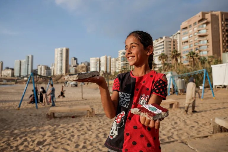 Displaced girl Nassim, 11, from Dahiyeh, shows off stones she painted during art activities set up by volunteers, in Beirut on October 16, 2024 [Louisa Gouliamaki/Reuters]