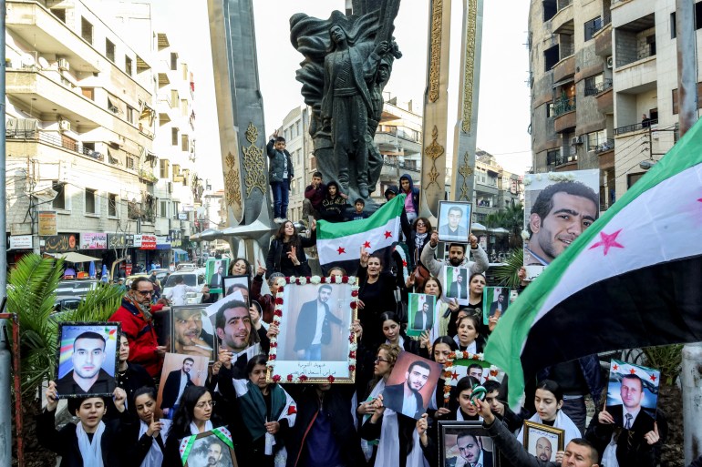 People gather with independence-era Syrian flags and pictures of 23 locals who died in Saydnaya and other Assad-regime prisons during a memorial vigil for them by the monument to the Great Syrian Revolt at al-Seyouf Square in Jaramana in the Damascus countryside on the city's outskirts on December 21, 2024. Islamist-led rebels took Damascus in a lightning offensive on December 8, ousting president Bashar al-Assad and ending five decades of Baath rule in Syria. (Photo by Shadi AL-DUBAISI / AFP)