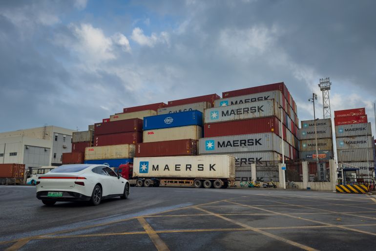 SHENZHEN, CHINA - APRIL 11: A white electric car drives past stacked Maersk shipping containers at a logistics yard near Yantian International Container Terminals, one of China's major maritime gateways for international trade, on April 11, 2025 in Shenzhen, China. China has imposed a new round of retaliatory tariffs on U.S. imports, raising duties to 125% in response to the latest escalation by the United States, which increased tariffs on Chinese goods to 145%. The growing trade tensions have further impacted China's export sector, affecting key industries such as logistics, manufacturing, and cross-border e-commerce. The measures are part of Beijing's broader strategy to counter rising economic pressure and defend its trade interests. (Photo by Cheng Xin/Getty Images)