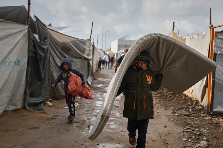 أطفال ينقلون فرشاتهم وأغطيتهم من الخيمة التي اغرقتها المياه بفعل الامطار (AP)