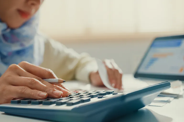 Closeup Asian muslim woman with hijab using tablet calculator focus on utility bills calculate check credit card receipt monthly expense bill in living room at house. Home financial lifestyle concept.