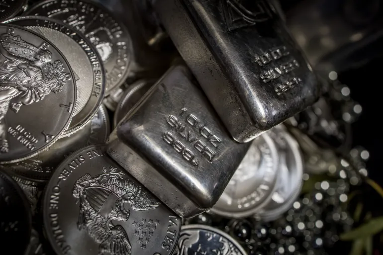 Multiple stacks of 10 ounce Silver bullion Ingot bars and 1 ounce Silver dollar coins among piles of silver ball bearings against a black background featuring the 2016 American Eagle US one dollar coin, the 2021 South African Krugerrand, the 2021 Australian Kangaroo, the 2013 Weiner Philharmonika, the 2020 Scottsdale Reserve Lion and the 2020 Sunshine Minting flying Eagle