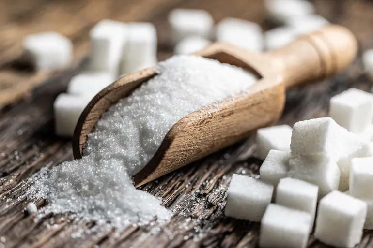 Granulated sugar in a wooden scoop or bowl on an old oak table.