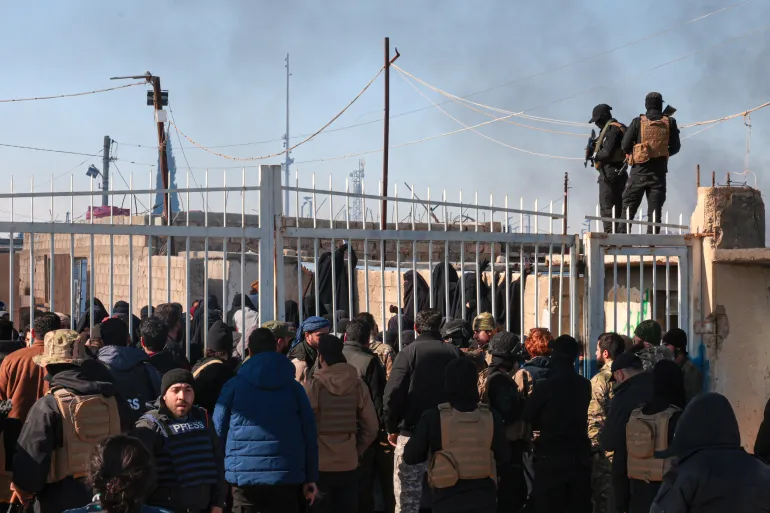 epa12667464 Members of the Syrian security forces stand in front of the gate of the Al-Hol camp, which houses families of suspected Islamic State (IS) group fighters, after the Syrian government took control of the area, in Hasakeh province, Syria, 21 January 2026. According to the Syrian Interior Ministry, security forces have entered al-Hol camp in Hasakah province to maintain stability following the withdrawal of Kurdish-led Syrian Democratic Forces (SDF) units and the temporary lack of guard presence. EPA/MOHAMMED AL-RIFAI