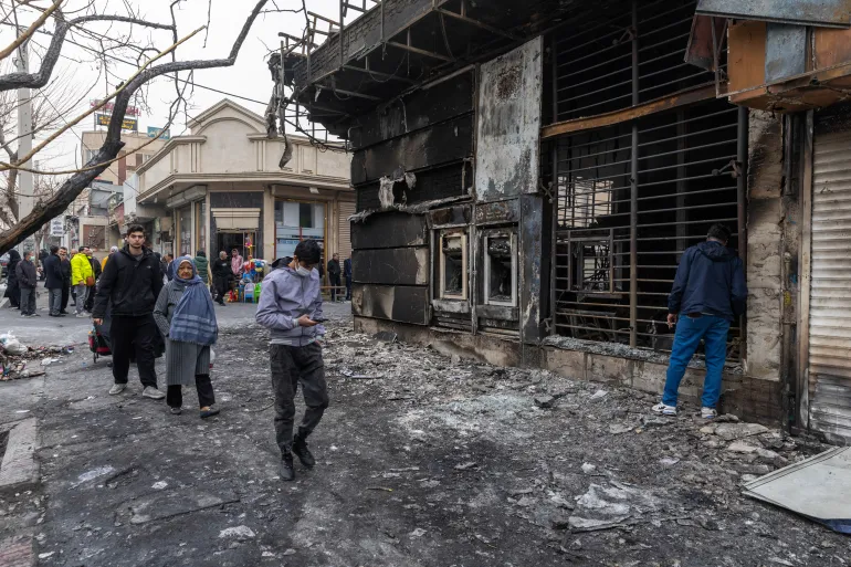 TEHRAN, IRAN - JANUARY 10: Pedestrians pass a burned out building on January 10, 2026 in Tehran, Iran. Some areas of Tehran sustained heavy damage during ongoing protests that came to a head on January 8, amid a growing economic and political crisis sweeping the country. (Photo by Stringer/Getty Images)