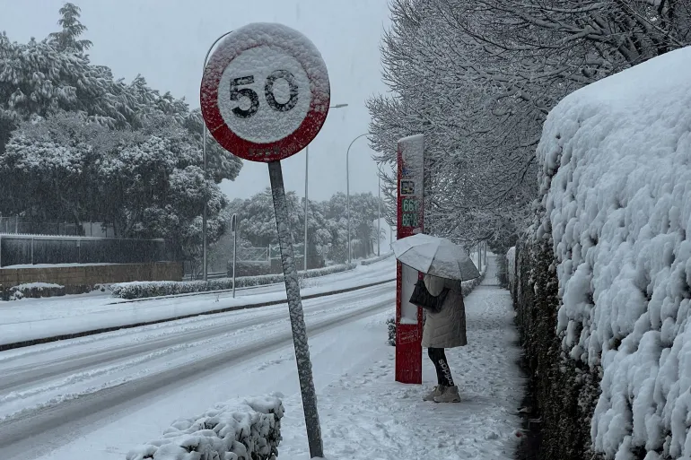 A woman holds an umbrella to protect herself while waiting for a bus as storm Kristin hits several parts of Spain and Portugal, in Galapagar, on the outskirts of Madrid, Spain, January 28, 2026. REUTERS/Silvio Castellanos