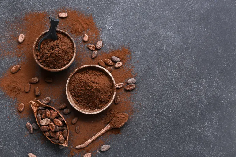 Bowls with cocoa powder and beans on black background