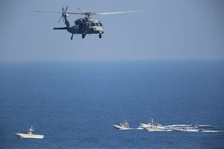 FILE - A U.S. MH-60 Seahawk helicopter flies over Iranian Revolutionary Guard patrol boats in the Strait of Hormuz on Dec. 21, 2018. The U.S. military is considering putting armed personnel on commercial ships traveling through the Strait of Hormuz, in what would be an unheard of action aimed at stopping Iran from seizing and harassing civilian vessels, four American officials told The Associated Press on Thursday, Aug. 3, 2023. (AP Photo/Jon Gambrell, File)