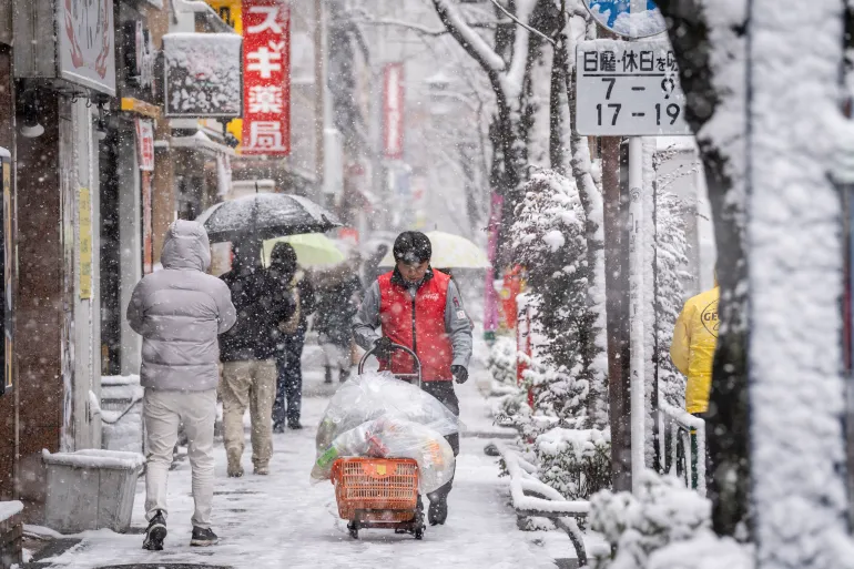A worker pushes a cart loaded with garbage bags through falling snow in Tokyo on February 8, 2026. (Photo by Yuichi YAMAZAKI / AFP)