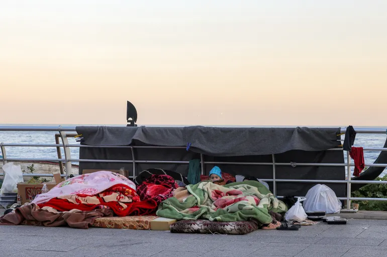 A boy looks on while lying under a blanket alongside family belongings in a makeshift encampment along the waterfront in Beirut on March 10, 2026, as civilians who fled the city's southern suburbs due to Israeli bombardment remain displaced.
