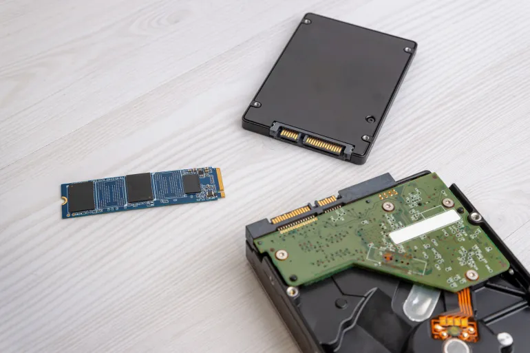 M2 SSD drive placed near SATA SSD and opened hard disk drive on light wooden desk, computer storage components comparison