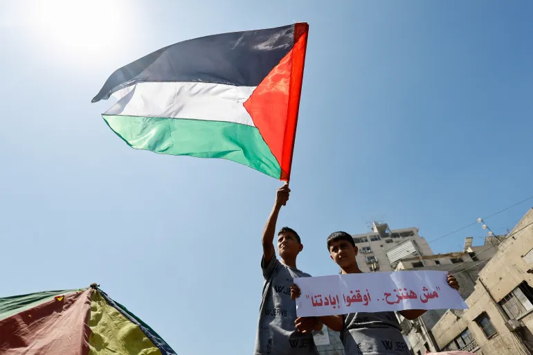 نزوح غزة A boy waves a Palestinian flag while another holds a sign that reads: "We will not be displaced. Stop our extermination", as Palestinians, refusing to move to the south, protest against an evacuation order by the Israeli military, amid an Israeli operation, in Gaza City, September 9, 2025. REUTERS/Mahmoud Issa