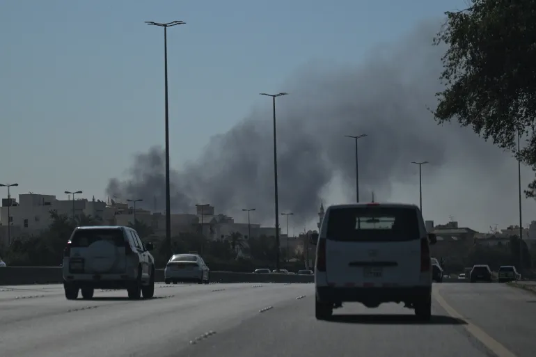 Motorists drive along a street as smoke rises from a reported Iranian strike in the area where the US Embassy is located in Kuwait City on March 2, 2026.