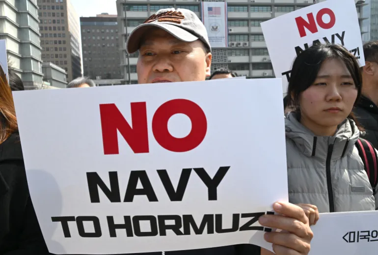 South Korean protesters hold placards during a protest against Trump's request to dispatch warships to the Strait of Hormuz in front of the US embassy in Seoul on March 16, 2026.