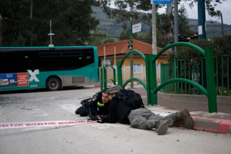 Israeli security forces take cover during a siren alert while gathering at the site of a Hezbollah missile strike that targeted a bus in the northern Israeli border town of Kiryat Shmona on March 23, 2026.