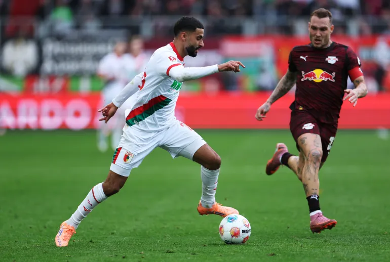 AUGSBURG, GERMANY - OCTOBER 25: Elias Saad of Augsburg is challenged by David Raum of RB Leipzig during the Bundesliga match between FC Augsburg and RB Leipzig at WWK-Arena on October 25, 2025 in Augsburg, Germany. (Photo by Adam Pretty/Getty Images)