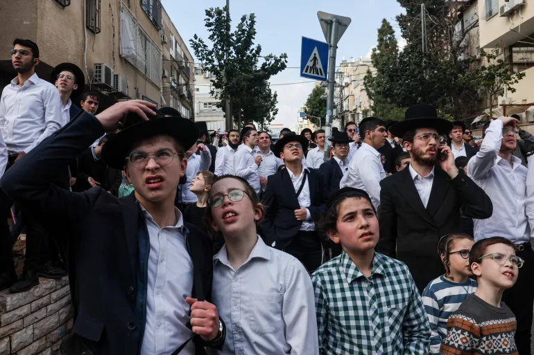 People gather outside a damaged building following an Iranian projectile strike, amid the U.S.-Israeli conflict with Iran, in central Israel, March 15, 2026. REUTERS/Tyrone Siu