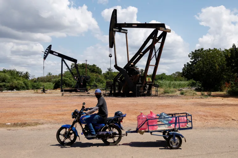 FILE PHOTO: A man on a motorcycle transports water bottles past pumpjacks, beside deteriorating oil infrastructure on the shores of Lake Maracaibo, where years of neglect have left rusted pipelines and oil slicks amid concerns raised by fishermen and locals that new private investment in Venezuelan state oil company PDVSA could further harm the fragile ecosystem, in Cabimas, Venezuela, January 26, 2026. REUTERS/Leonardo Fernandez Viloria/File Photo