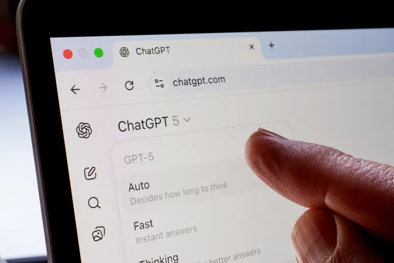 Finger points at ChatGPT 5 model selector on chatgpt.com, showing Auto, Fast and Thinking modes on a laptop screen. Stafford, United Kingdom, August 21, 2025