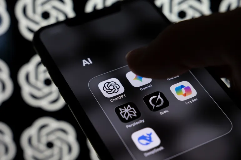 A smartphone screen displays a folder containing the AI applications Claude, ChatGPT, Gemini, Perplexity, Grok, Copilot, and DeepSeek with a multitude of OpenAI logos in the background. OpenAI announces the release of GPT-5.3-Codex, its most advanced agentic coding model to date, in Creteil, France, on February 6, 2026. (Photo by Samuel Boivin/NurPhoto via Getty Images)