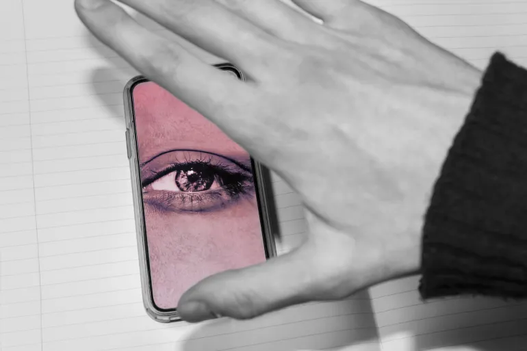 hand trying to close the screen of the smartphone with watching eye. smartphone is spying on the user. Smartphones overhear and spy, selective focus