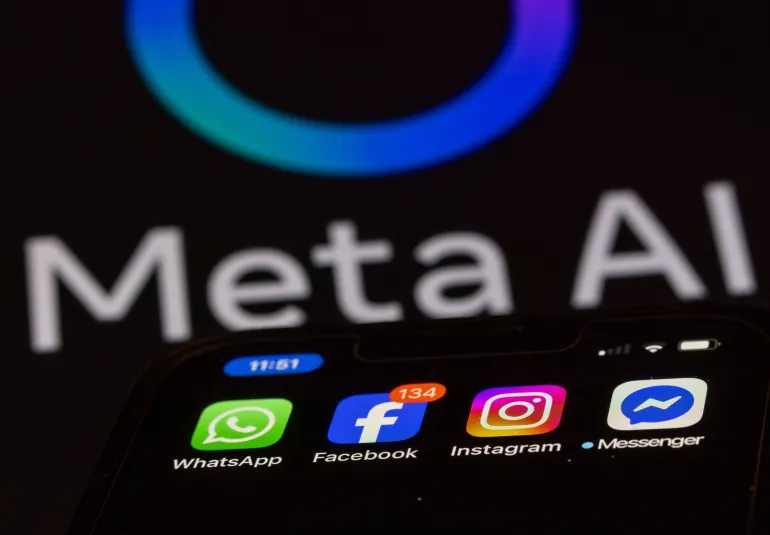 ILLUSTRATION - 27 May 2025, Mecklenburg-Western Pomerania, Schwerin: The Facebook, Messenger, Instagram and WhatsApp apps are shown on a smartphone display, with a monitor with the logo of the AI application Meta AI in the background. The Facebook group Meta can now start training its artificial intelligence systems on a large scale with user data from Germany. Photo: Jens Büttner/dpa (Photo by Jens Büttner/picture alliance via Getty Images)