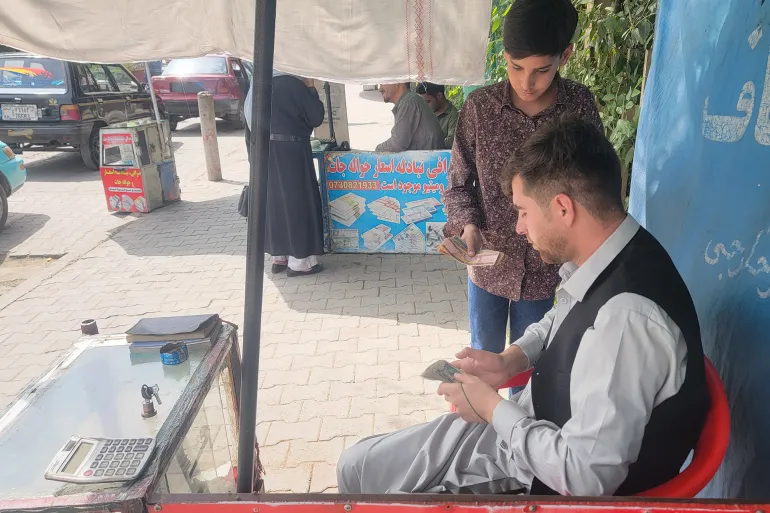 _صراف يتعامل مع أحد العملاء في كابل وسط حركة نشطة للسوق.
