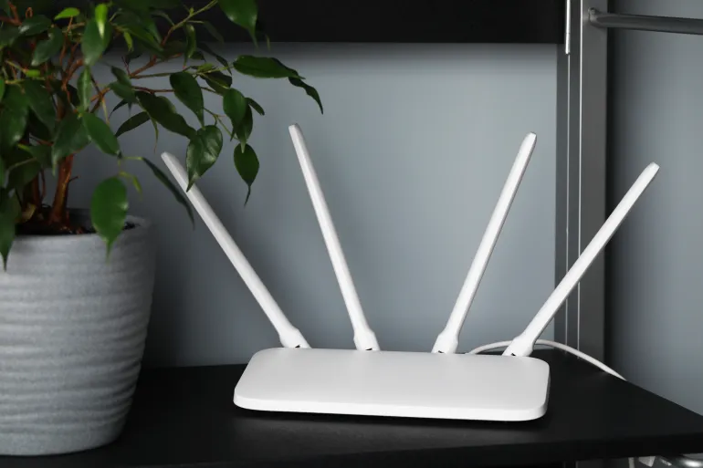 New white Wi-Fi router near potted plant on black shelf