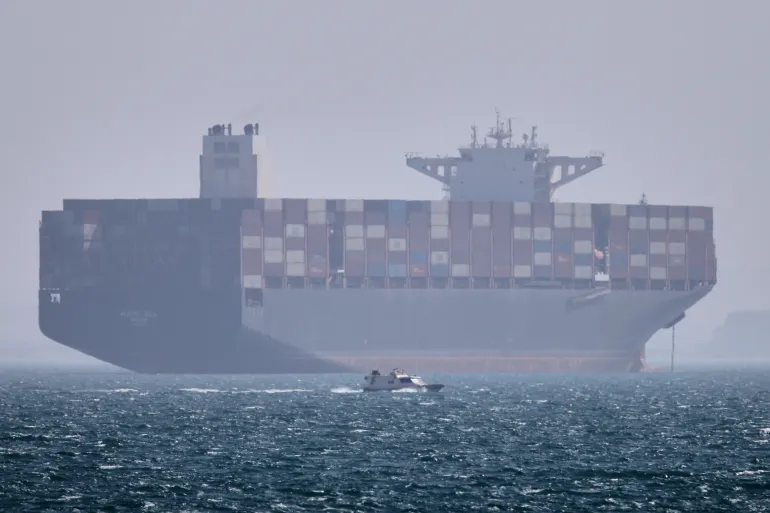 A container ship sits at anchor as a small motorboat passes in the foreground in the Strait of Hormuz off Bandar Abbas, Iran, Saturday, May 2, 2026. (Amirhosein Khorgooi/ISNA via AP)