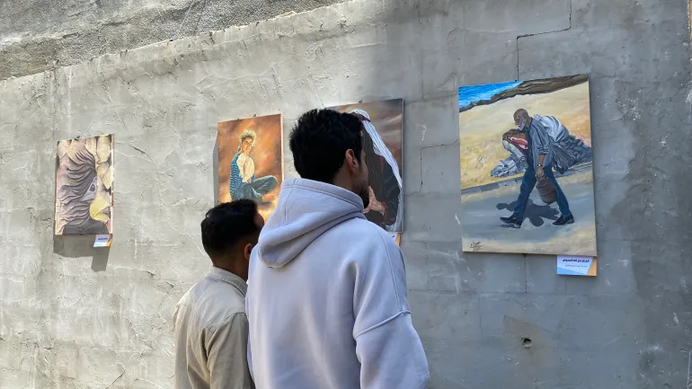 زائر لمعرض "ما تركته النجاة" يتأمل لوحة تصور النزوح والتهجير القسري / رائد موسى / مخيم البريج وسط قطاع غزة / الجزيرة نت.