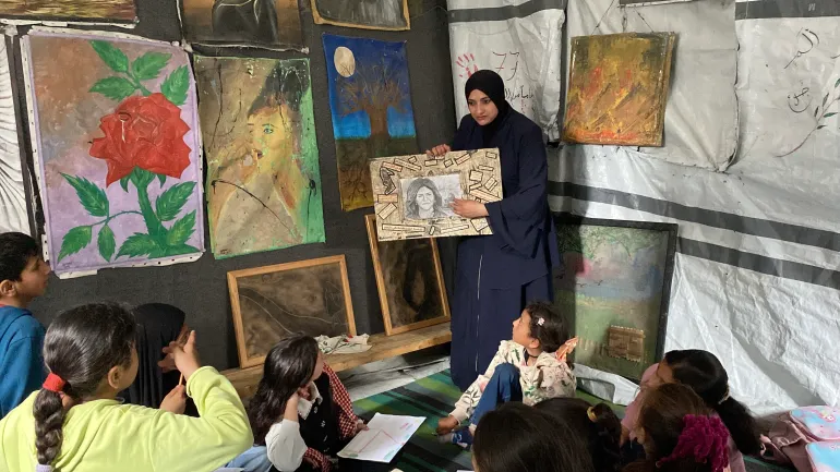 الفنانة أحلام عبد العاطي تستخدم لوحة للراحلة الشهيدة شيرين أبو عاقلة لشرح درس فني لمجموعة من الأطفال النازحين / رائد موسى / خان يونس / الجزيرة نت.