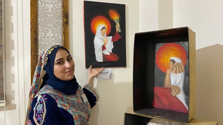 الفنانة سيرين سمرة تعرض أحد لوحاتها المشاركة في معرض "ما تركته النجاة" / رائد موسى / مخيم البريج وسط قطاع غزة / الجزيرة نت.