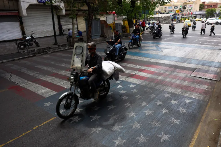 An Iranian rides his moped across a painted depiction of the US flag on a street in the south of Tehran on May 5, 2026.
