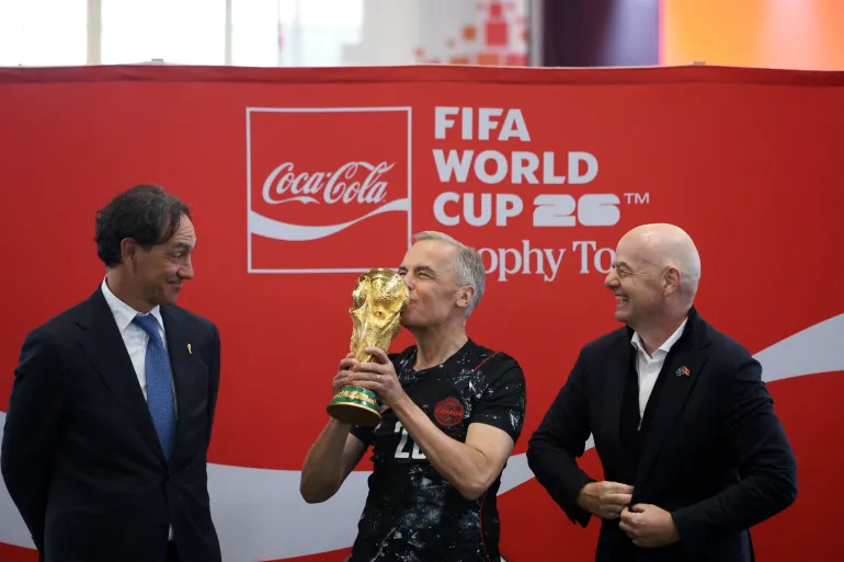 Canada's Prime Minister Mark Carney (C) kisses the FIFA World Cup Trophy, as FIFA President Giovanni Infantino (R) and Italian football coach Alessandro Nesta look on, during a FIFA & Coca Cola World Cup Trophy Tour at Park Landsdowne Stadium in Ottawa, Canada, on May 24, 2026.