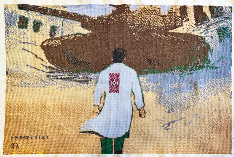 تطريز من عمل بسمة ناطور لرسم توضيحي لمحمود عباس للدكتور حسام أبو صفية وهو يتجه نحو دبابة إسرائيلية (بإذن من متحف فلسطين بأمريكا)
