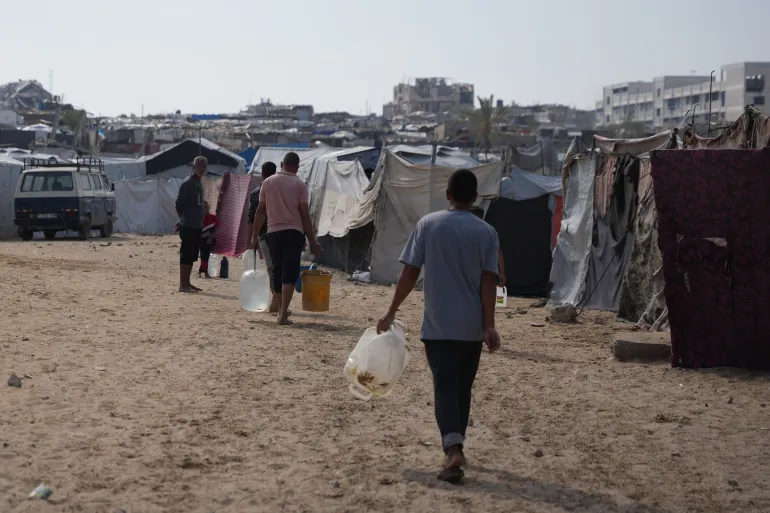 Displaced Palestinian carry jerrycans filled with water through a tent camp in Khan Younis, in the southern Gaza Strip, Thursday, April 30, 2026. (AP Photo/Abdel Kareem Hana)