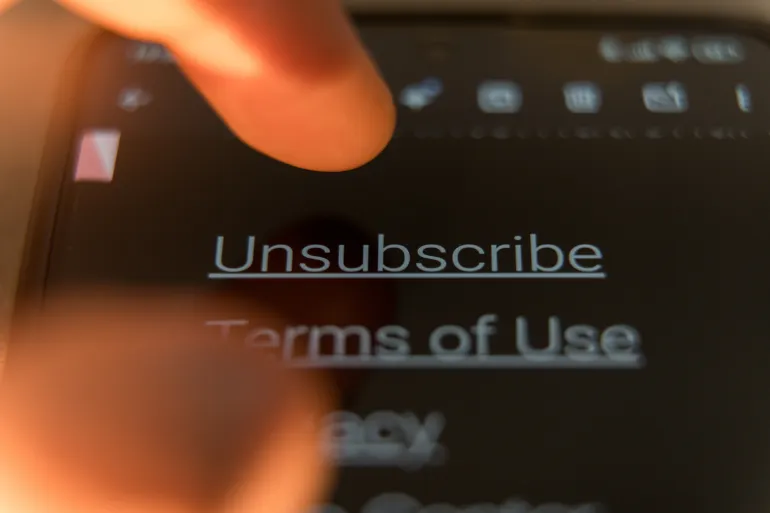 Close-up of a finger to tap the Unsubscribe link on a smartphone screen in dark mode. High quality photo