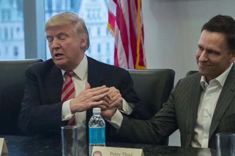 U.S. President-elect Donald Trump, left, speaks while Peter Thiel, billionaire co-founder of PayPal Inc. and a member of Donald Trumps transition team, listens during a meeting with technology leaders at Trump Tower in New York, U.S., on Wednesday, Dec. 14, 2016. Technology industry leaders met with Trump seeking to persuade a man whose presidential bid many of them opposed to avoid policies they believe would hurt their companies. Im here to help you folks do well, Trump told the executives as the meeting began. Photographer: Albin Lohr-Jones/Pool via Bloomberg
