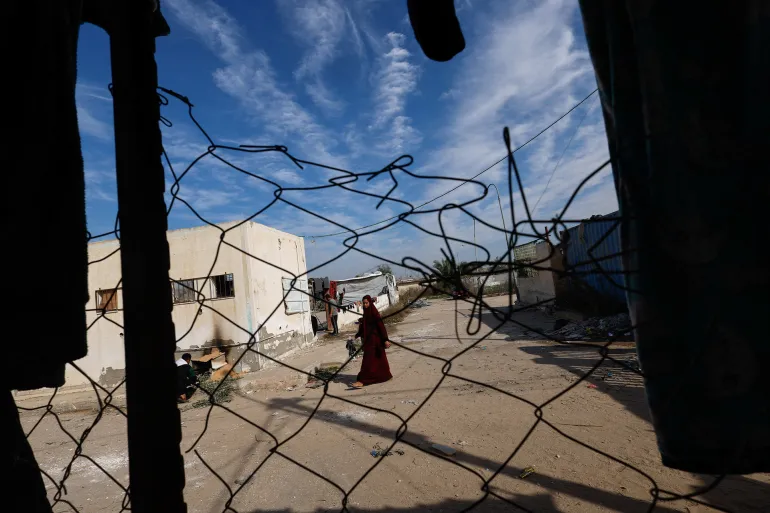 A woman walks as displaced Palestinians who fled their homes due to Israeli strikes shelter at Rafah crossing on the border with Egypt, amid the ongoing conflict between Israel and the Palestinian Islamist group Hamas, in Rafah in the southern Gaza Strip, December 8, 2023. REUTERS/Mohammed Salem