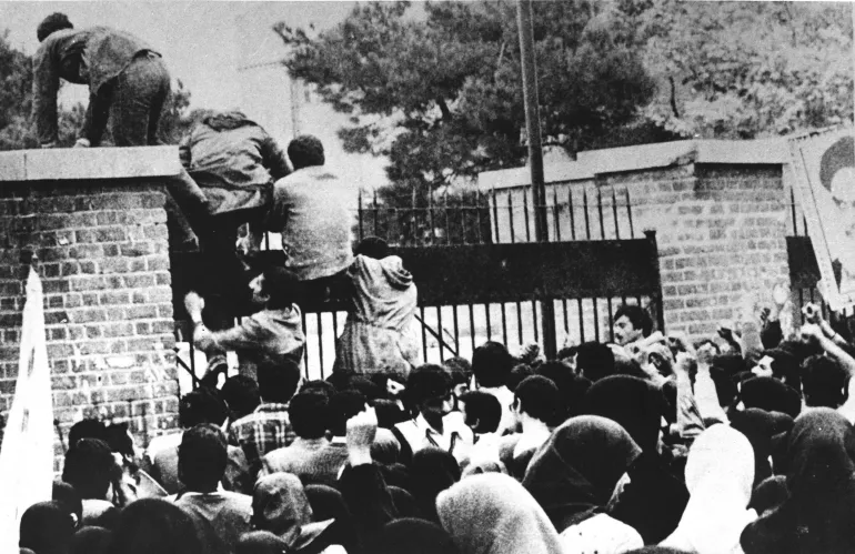 طلابٌ إيرانيون يتسلقون جدار السفارة الأميركية في طهران، 4 نوفمبر/تشرين الثاني 1979. وبعد عشرين عامًا، في 4 نوفمبر/تشرين الثاني 1999، صار مبنى السفارة السابق يُخرّج ضباطًا من الحرس الثوري للجمهورية الإسلامية. (الفرنسية)