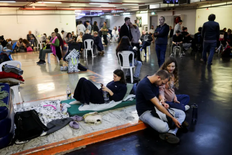 People take shelter in a parking lot during an Iranian strike, after Iran launched missile barrages following attacks by the U.S. and Israel on Saturday, in Tel Aviv, Israel March 1, 2026. REUTERS/Ronen Zvulun