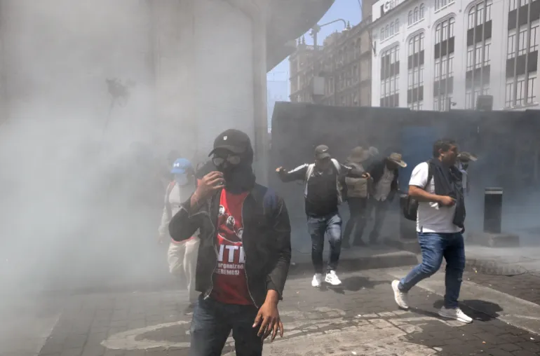 Teachers stand near a barricade blocking access to the Zocalo amid smoke after police actions during a demonstration ahead of the 2026 FIFA World Cup, in Mexico City on June 1, 2026. (Photo by Alfredo ESTRELLA / AFP)