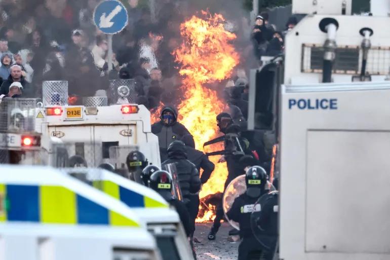 Protesters (behind) stand off with police as the former block a road leading to a hotel previously believed to house migrants, in Glengormley, north of Belfast, Northern Ireland, on June 10, 2026.