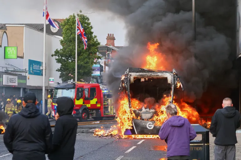 People watch as a vehicle burns during a protest in East Belfast following a stabbing incident in Belfast, Tuesday, June 9, 2026. (AP Photo/Peter Morrison)