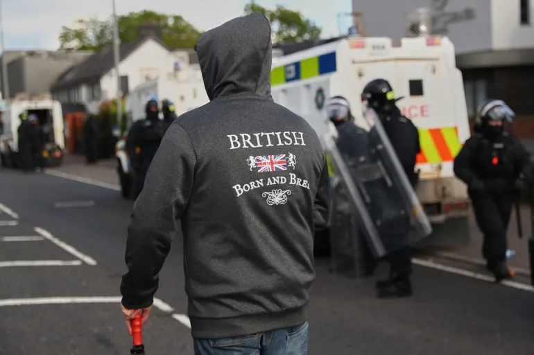 Police in riot gear watch protesters following near Newtownabbey, in Belfast, Northern Ireland, Wednesday, June 10, 2026, following a stabbing incident on Monday night. (AP Photo/Peter Morrison)