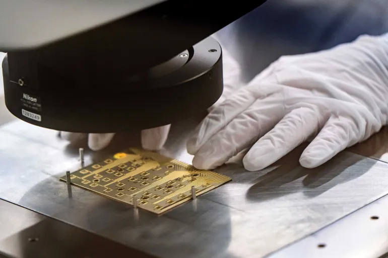 A gowned worker adjusts a test coupon for indium phosphide wafer certification testing in a Coherent manufacturing facility where lasers are developed for transmitting data among chips, which could decrease power use by AI systems, on Tuesday, June 16, 2026, in Sherman, Texas. Jensen Huang, president and CEO of Nvidia was at the facility with Coherent CEO Jim Anderson to break ground on an expansion of the building. (AP Photo/Jeffrey McWhorter)