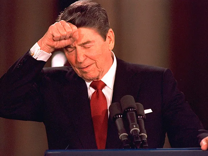 في هذه الصورة المؤرخة في 19 مارس/آذار 1987، يضرب الرئيس رونالد ريغان على جبينه ردًّا على سؤال أحد الصحفيين خلال مؤتمر صحفي أقر فيه بتورّط إسرائيل في قضية إيران-كونترا.